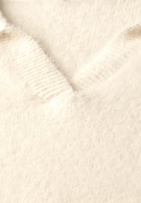 Maglione color crema con una texture morbida e pelosa. Presenta un collo a V e un bordo a coste. Il materiale appare caldo e leggero.