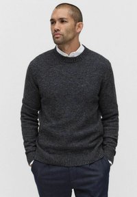 Ciemnoszary sweter dziany z okrągłym dekoltem, ściągaczami przy mankietach i u dołu. Noszony na koszuli z kołnierzykiem, posiadającej teksturowany materiał.