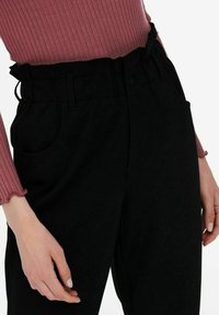 Černé kalhoty s vysokým pasem a šňůrkou v pase, se dvěma předními kapsami a hladkým povrchem. S kombinací s ribbovaným vínovým topem.