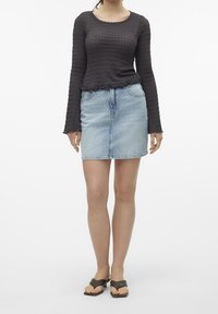 Svart texturerad långärmad topp, parat med en ljusblå denim minikjol. Modellen bär svarta platta sandaler. En enkel och avslappnad outfit.