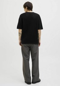 Black textured short-sleeve top with a loose fit, paired with gray wide-leg trousers and black footwear. The back shows tattooed arms.