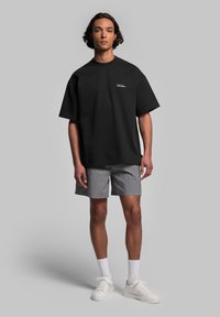 Svart oversized t-shirt i bomull, kortärmad, med logotyp fram. Matchad med randiga shorts i svart och vitt, vita sneakers.