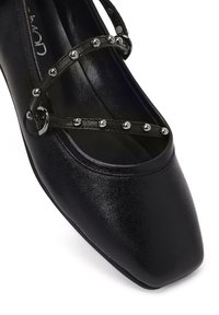 Scarpa nera con tacco alto e punta squadrata, caratterizzata da una tomaia in pelle lucida e borchie metalliche decorative lungo le cinghie incrociate.