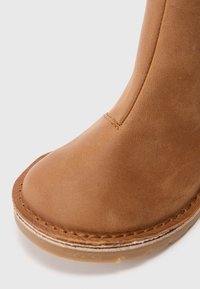 Botine din piele maro, cu vârf rotund, textură netedă, cusături contrastante și talpă din cauciuc cu o margine ușor translucidă.