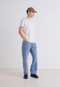 Fehér, rövid ujjas póló, világoskék, laza szabású farmernadrág, fekete sneaker és szürke sapka. Egyszerű dizájn, látható minták vagy logók nélkül.