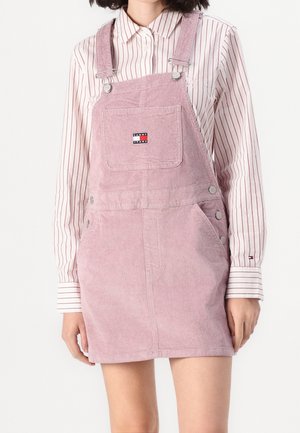 Kvinde iført lys pink kordnederdel med forlomme og stribet langærmet skjorte med krave og knapper.