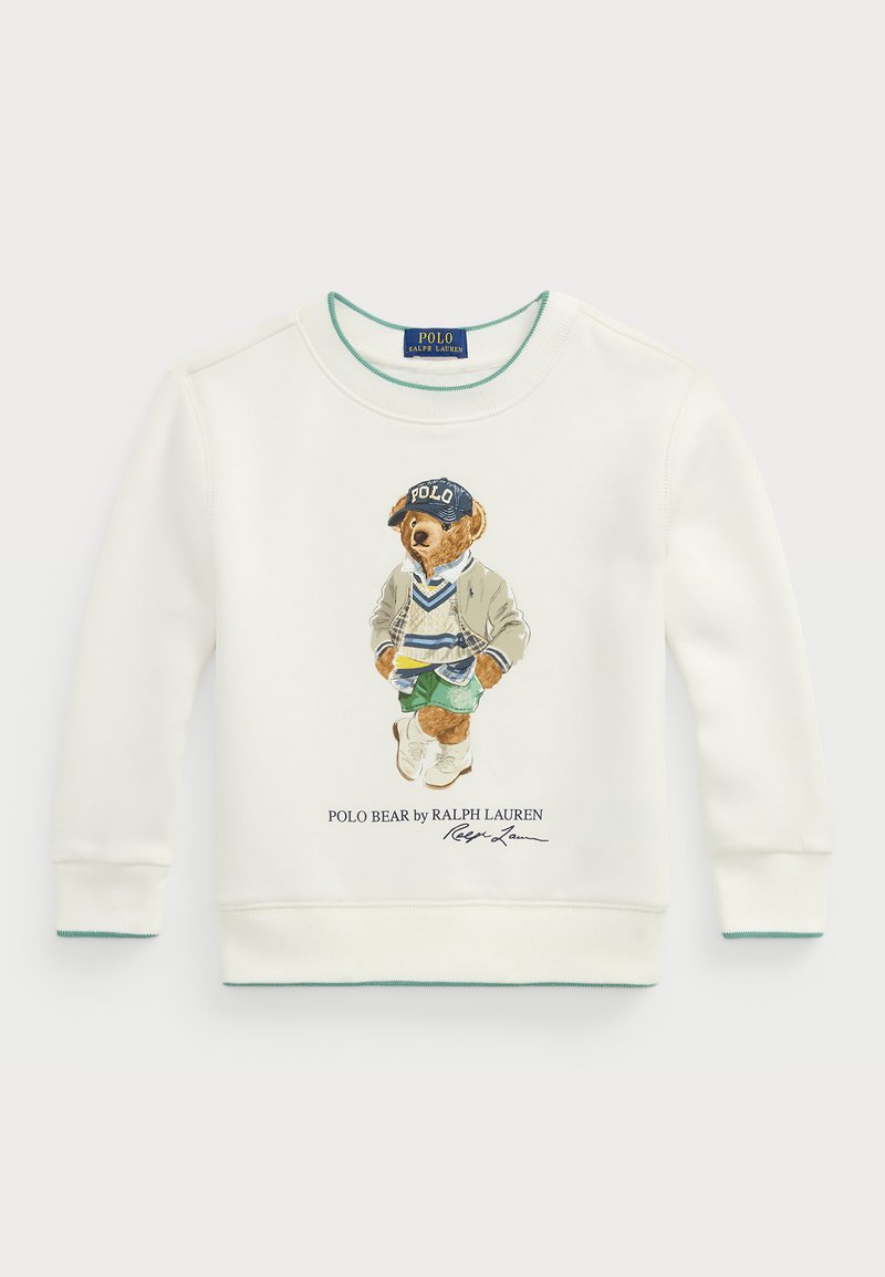 Sudadera blanca con un gráfico de un oso que lleva una gorra azul, pantalones cortos verdes y una chaqueta beige. Detalles en teal en el cuello y los puños.