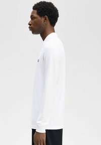 Polo a maniche lunghe bianco con logo ricamato nero sul petto. Presenta un collo con revers e polsini a coste. Materiale in cotone liscio.