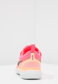 Bottines de sport rose vif et pêche vues de l'arrière, montrant un tissu en maille, un logo noir et une semelle blanche sur une surface blanche.