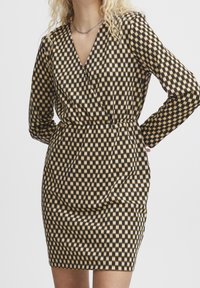 Musta ja beige ruudullinen mekko pitkät hihat, V-kaula-aukko, istuva vyötärö ja hieman poimullinen pinta hameessa.