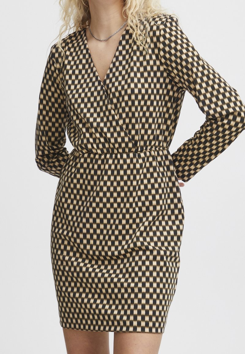 Musta ja beige ruudullinen mekko pitkät hihat, V-kaula-aukko, istuva vyötärö ja hieman poimullinen pinta hameessa.