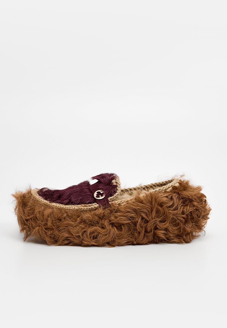 Braune, mit Fell gefütterte Hausschuhe mit einem geflochtenen Jute-Besatz, ausgestattet mit einem samtigen burgunderrot Akzent und einem dekorativen Knopf an der Seite.