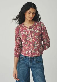 Cardigan floral framboise à manches longues, avec des poignets côtelés et un col rond, comportant une fermeture à boutons et des motifs floraux complexes.