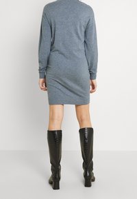 Grå stickad klänning med långa ärmar, figurnära passform och rund halsringning. Matchad med svarta klackade stövlar i croco-prägling som går upp till knäet.