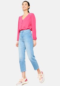 Blusa rosa de botones con mangas abullonadas, combinada con jeans rectos de mezclilla azul claro y zapatillas beige con acentos rosas.