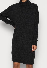 Svart polokragsklänning gjord av mjukt, texturerat tyg. Har en lös passform, långa ärmar och ribbade muddarna och fållen.