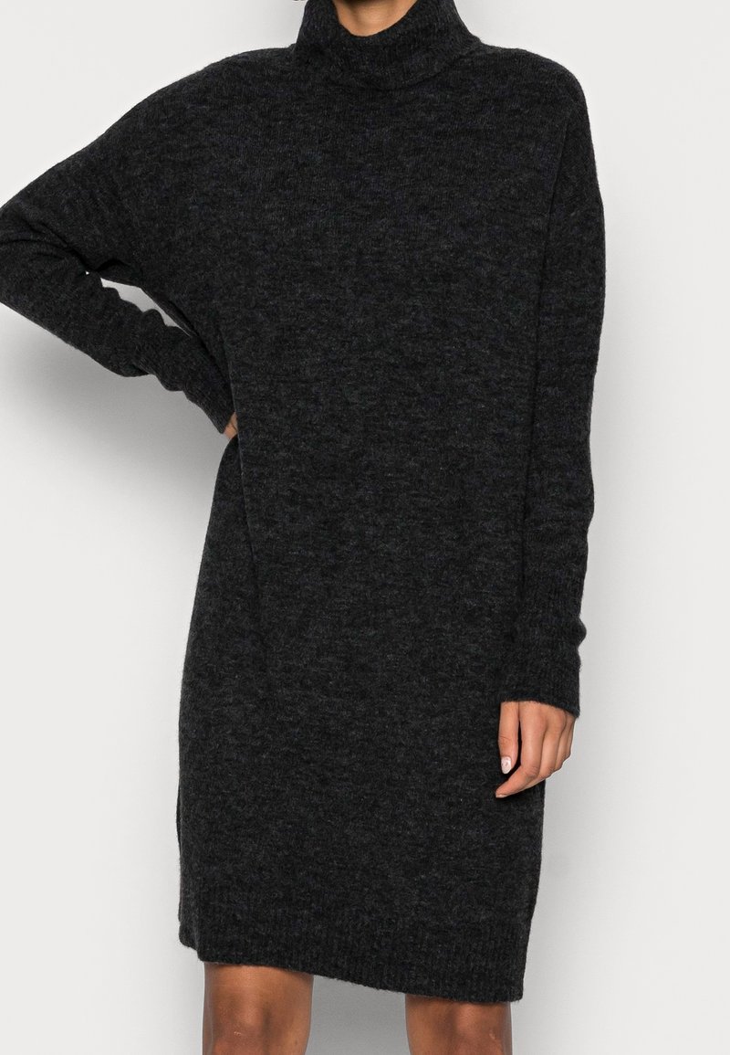 Svart polokragsklänning gjord av mjukt, texturerat tyg. Har en lös passform, långa ärmar och ribbade muddarna och fållen.