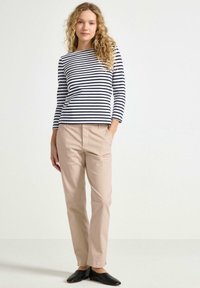 Pruhovaný dlouhý rukáv v námořnické modři a bílé barvě, v kombinaci s béžovými kalhotami rovného střihu a černými slip-on botami. Hladká látka s uvolněným střihem.