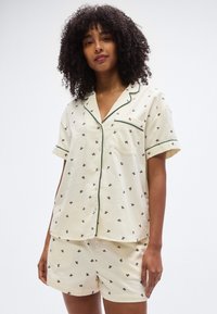 Σετ κοντών πυτζάμων από κρεμ βαμβάκι, με τοπάν  κουμπωτό με πράσινη επένδυση και μικρά λουλουδάτα σχέδια, συνδυασμένο με σορτς στο ίδιο σχέδιο.