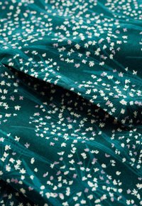 Teal fabric with a floral pattern featuring white and pale purple small foliage elements, showcasing a smooth texture and soft drape.