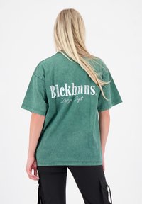 Groen oversized t-shirt met korte mouwen, voorzien van witte tekst op de achterkant. Gemaakt van katoen met een licht vervaagde afwerking.