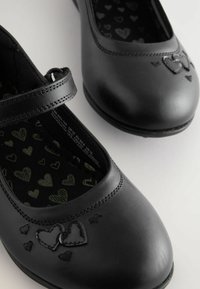Chaussures Mary Jane noires en cuir, avec un bout rond, dotées d'une sangle, d'une couture en forme de cœur et d'un intérieur imprimé avec de petits cœurs.