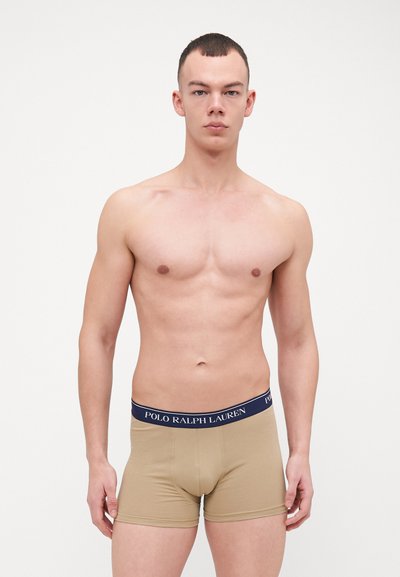 Beige bokseri aluskleidid, mis on valmistatud pehmest materjalist, millel on tume sinine elastne vöökoht, millel on trükitud "POLO RALPH LAUREN" logo.