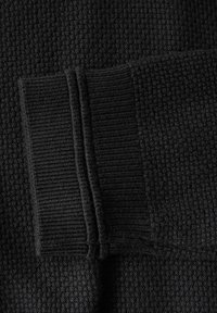 Svart stickad tyg med strukturerad våffelmönster, som har en ribbad muddsektion med två vertikala sömmar. Mjukt, material av medelvikt.