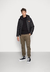 Black puffer jacket with a hood and quilted texture, paired with a black sweatshirt, olive cargo pants, and black high-top sneakers.