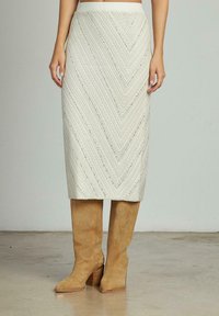 Jupe midi crème avec un motif en chevron et des détails texturés ; associée à des bottes en suède beige jusqu'aux genoux avec un talon bloc.