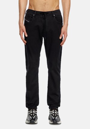 Joggeurs en denim noir avec une taille à cordon, deux poches avant et un design ajusté. Le tissu a une texture lisse. Accompagnés de baskets.