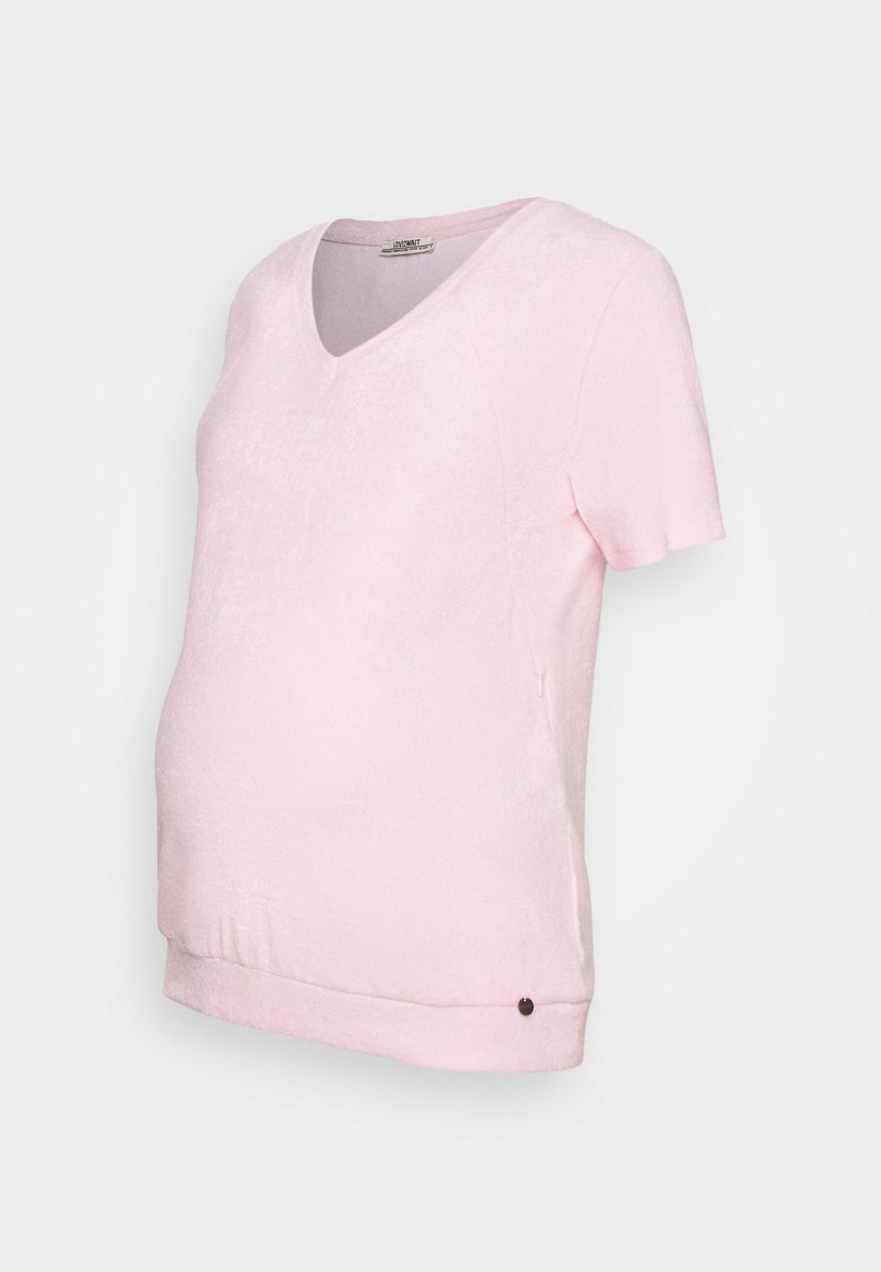 T-shirt de maternidade rosa claro com decote em V, mangas curtas e bainha curvada. O tecido tem uma textura suave, apresentando um pequeno botão de acabamento na parte inferior.