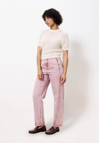 Leichter, cremefarbener, gestrickter Pullover mit kurzen Ärmeln, kombiniert mit hochgeschnittenen, hellrosa geraden Jeans und braunen Slippern.
