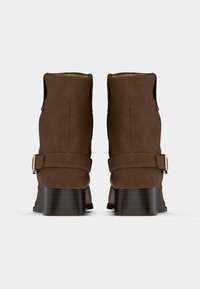 Brūnas zamša potītes zābaki ar apaļu purngalu, zemu sakrautu papēdi un dekoratīvu siksnu ar zelta sprādzes detaļu. Vienkāršs, gluds dizains.