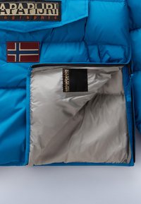 Blauwe pufferjack met een rood Noorwegen vlagpatch en een merklogo. De binnenkant heeft een gladde zilveren voering en een ritszak.