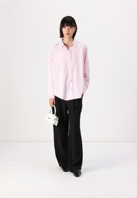 Camicia a righe rosa e bianche con bottoni, pantaloni neri a gamba larga e una piccola borsa bianca; tessuto morbido e vestibilità rilassata.