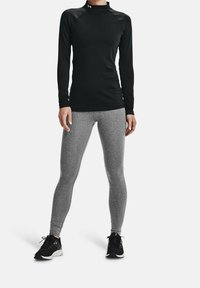 Musta pitkähihainen urheilu-paita, jossa on korkea kaulus, yhdistettynä harmaisiin legginsseihin ja mustiin lenkkareihin, joissa on valkoisia yksityiskohtia ja nauhoja.