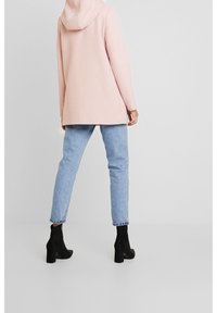 Cappotto cappuccio rosa chiaro con una vestibilità comoda, abbinato a jeans azzurri e stivaletti neri con tacco. Design semplice, texture morbida.