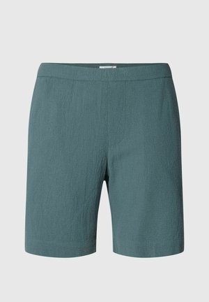 Vidēja garuma viendabīgas tirkīzzilas šorti ar teksturētu audumu un elastīgu jostu, uz vienkārša gaiša fona.