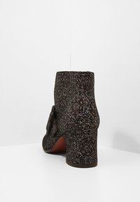 Botín oscuro texturizado que presenta un tacón bloque y un detalle de lazo en el costado, con un patrón moteado en tonos de gris y marrón.