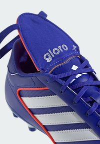 Botas de fútbol azules con acentos en blanco y rojo. Presentan una parte superior sintética texturizada, lengüeta acolchada y diseño tradicional de cordones.