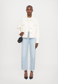 Giacca di denim bianca, jeans azzurri a gamba larga con orli sfrangiati, tacchi neri a punta e una piccola borsa nera trapuntata con tracolla a catena.