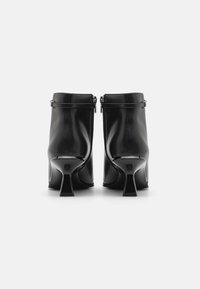 Bocanci negri din piele la gleznă cu o textură netedă, închidere cu fermoar și un toc stiletto distinctiv, curbat. Design simplu cu accente minime.