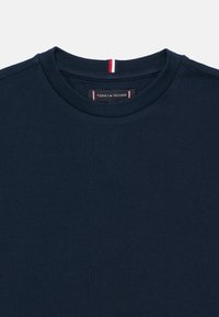 T-shirt de algodão azul marinho com decote redondo, apresentando um pequeno detalhe vermelho, branco e azul na parte de trás do pescoço; etiqueta visível por dentro.