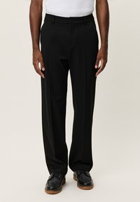 Μαύροι ραμμένοι παντελόνες με ίσια γραμμή, κατασκευασμένοι από λείο ύφασμα, με κλείσιμο με κουμπί και θηλιές για ζώνη, φορεμένοι με μαύρα παπούτσια.