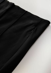 Zwart stoffen item met plooien; heeft een klein verborgen zakje en een gladde textuur. Netjes gevouwen tegen een lichte achtergrond.
