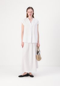 Haut blanc à manches courtes avec un décolleté en V, associé à une longue jupe blanche fluide. Des ballerines noires et un sac tissé complètent la tenue.