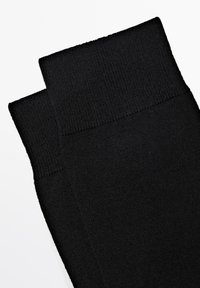 Sorte knæhøje sokker med ribbet tekstur øverst og glat materiale. Designet til holdbarhed og komfort i en klassisk stil.