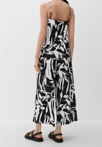Robe à motifs noir et blanc avec jambes larges et fines bretelles, en tissu plissé. Associée à des sandales noires à lanières.