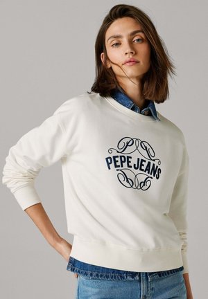 Crèmekleurige sweatshirt met geribbelde manchetten en zoom, met daarop een marineblauw "PEPE JEANS" logo in sierlijke letters, gedragen over een denim blouse.